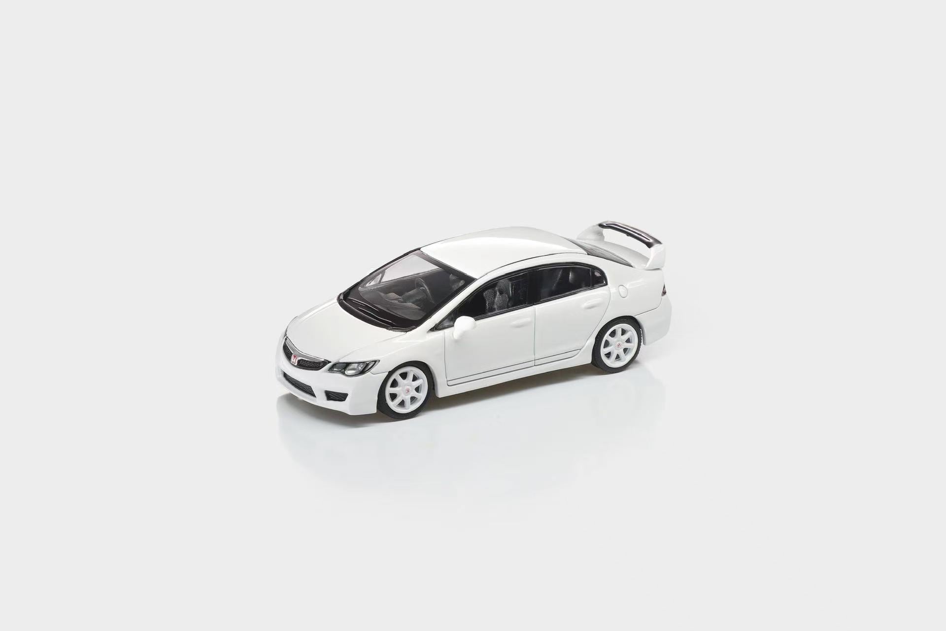 A white die-cast model car, resembling a Honda Civic, shown from a three-quarters front angle on a light gray reflective studio background.