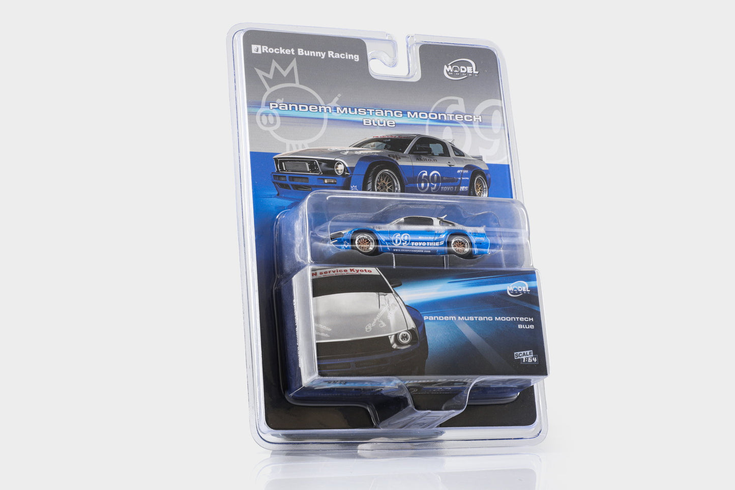 A packaged die-cast model car of a blue 1969 Mustang Monte Carlo race car, shown in its original blister pack with a card insert on a light gray background.