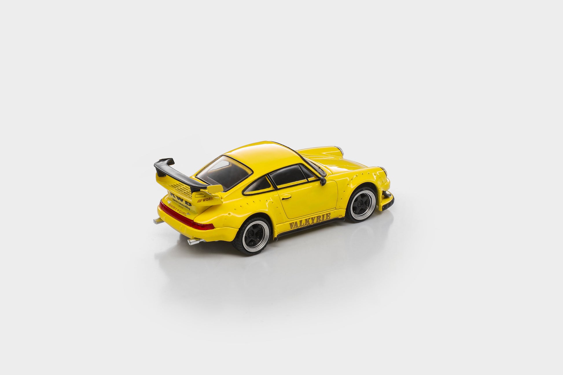 A bright yellow diecast model car with a black rear spoiler and black wheels, shown from a three-quarters rear angle on a light gray background.