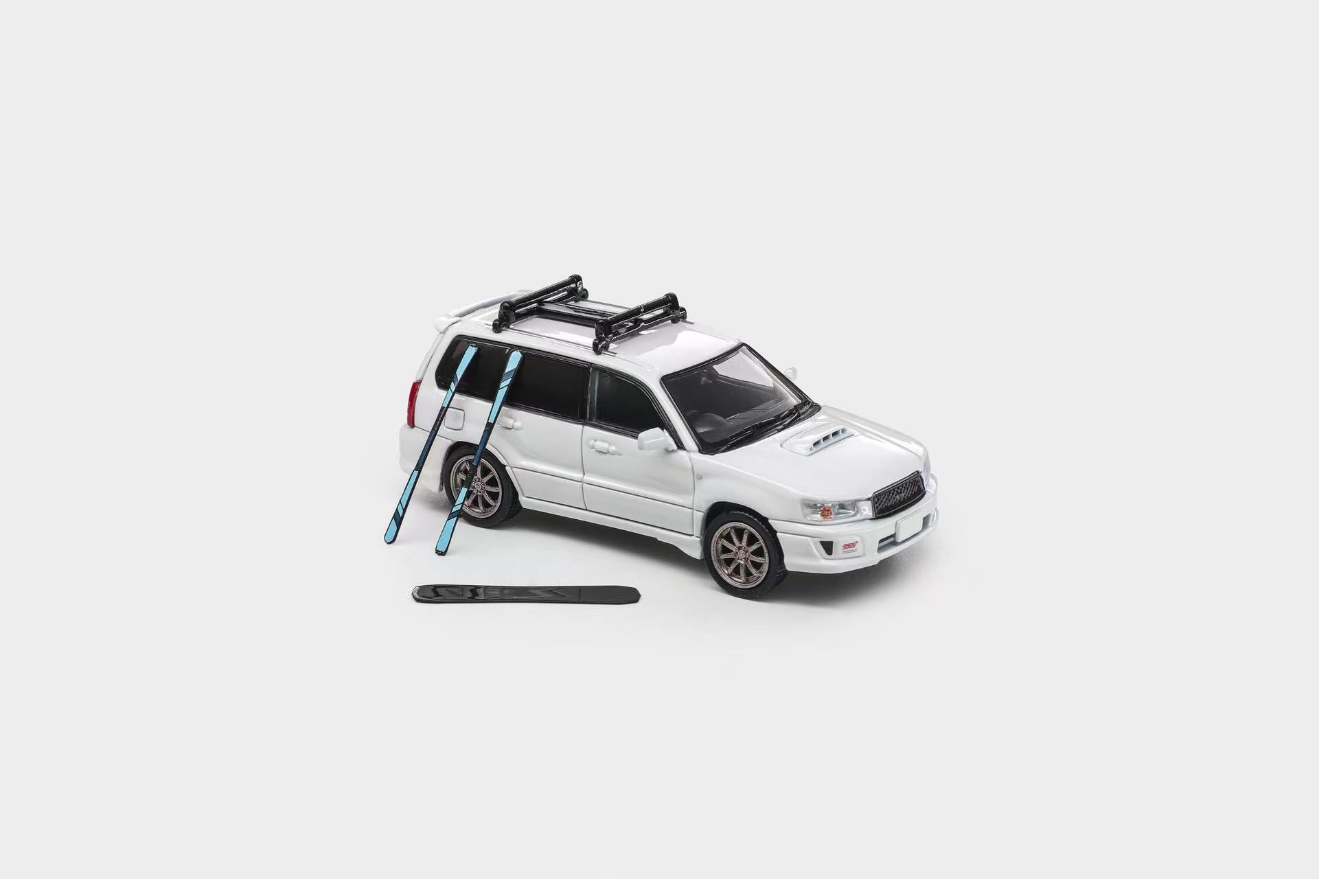 A white die-cast model SUV with a black roof rack, shown on a light gray background with two blue skis and a black ski boot placed beside it.