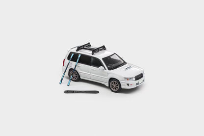 A white die-cast model SUV with a black roof rack, shown on a light gray background with two blue skis and a black ski boot placed beside it.