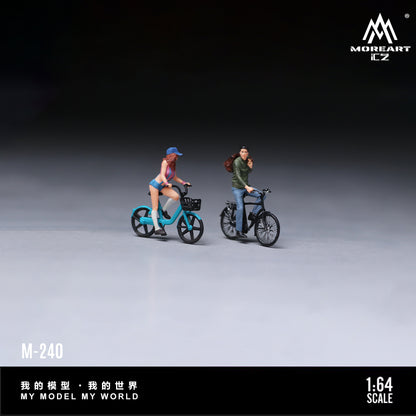 MoreArt 1:64 Cycling Couple Figure Set M-240 displayed in a clean studio scene featuring two miniature cyclist figures with detailed bicycles, perfect for 1:64 scale diecast model car dioramas, city layouts and miniature collections.