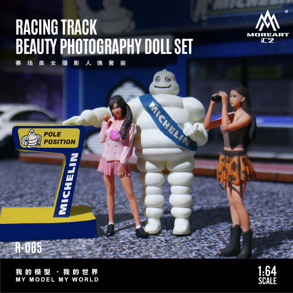 A 1:64 scale collectible doll set featuring a racing track beauty photographer theme, including a Michelin-themed white tire mascot with a blue sash, two female dolls in pink and brown outfits, a yellow and blue number 7 pole sign, and a black background with Chinese text and the Morialt brand logo.