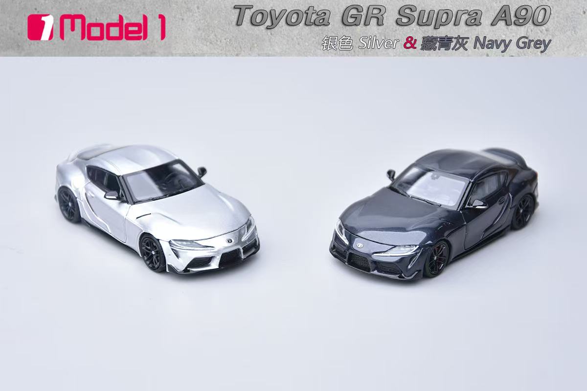 Two toy model cars, one silver and one navy gray, on a light gray background with 'Toyota GR Supra A90' text.