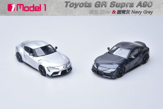Two toy model cars, one silver and one navy gray, on a light gray background with 'Toyota GR Supra A90' text.
