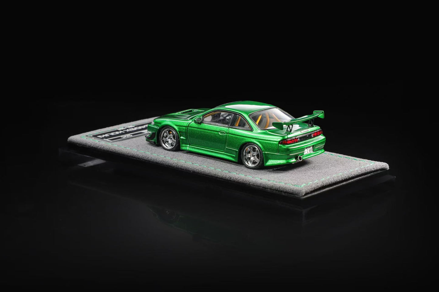 A metallic green die-cast model car displayed on a textured gray base against a solid black background.