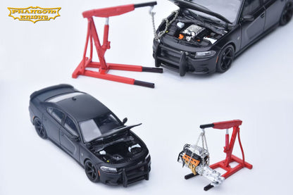 A set of miniature model cars and an engine hoist set on a white background. The set includes a black die-cast Dodge Charger with its hood open, a smaller black car, a red engine hoist, and a miniature engine hanging from a chain.