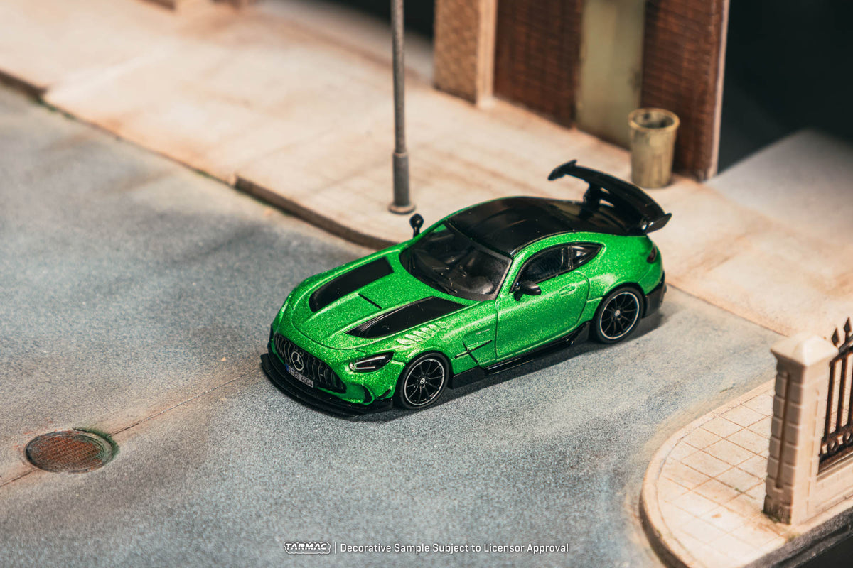 Green toy car on a miniature street with buildings in the background