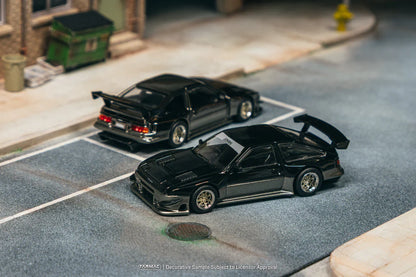 Two black model cars on a miniature street with buildings in the background