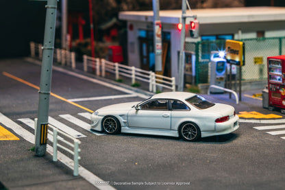 White car on a city street with traffic lights and buildings in the background