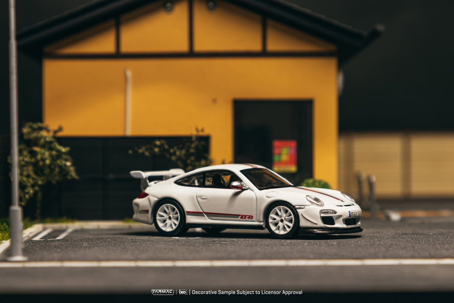 White sports car with red accents parked on a street in front of a yellow building.