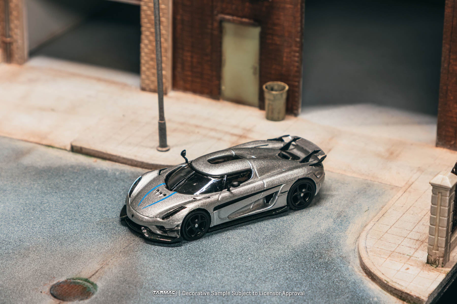 Model car on a miniature street with buildings and a trash can in the background