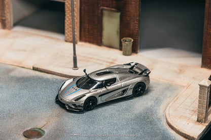 Model car on a miniature street with buildings and a trash can in the background