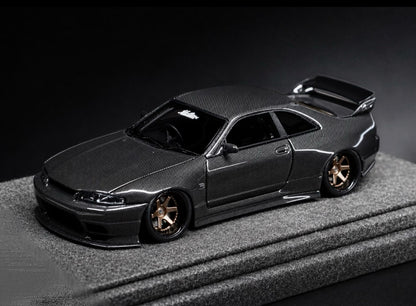 A dark gray carbon-fiber replica model of a Nissan Skyline R33 GT-R, displayed on a textured gray platform against a dark studio background.
