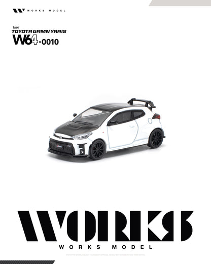 A 1/64 scale model of a Toyota Gamin Yaris W640010 by Works Model, shown as a white and black car with a carbon fiber hood and roof, on a white background with brand logos.