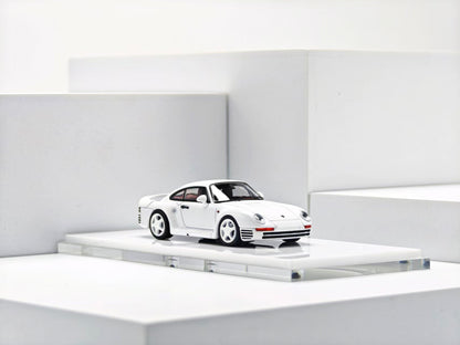 A miniature white Porsche 911 model car displayed on a clear acrylic platform against a minimalist white geometric background.