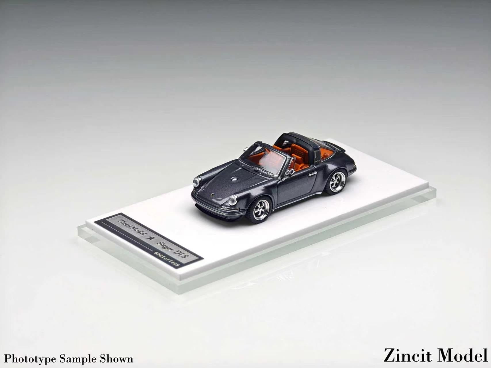 A miniature model of a dark gray convertible Porsche 911, displayed on a clear acrylic stand with a label, against a neutral gray background.
