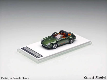 A miniature green Porsche 911 Targa model car with a black soft top and orange-brown interior, displayed on a clear acrylic stand with a label, photographed on a neutral gray gradient background.