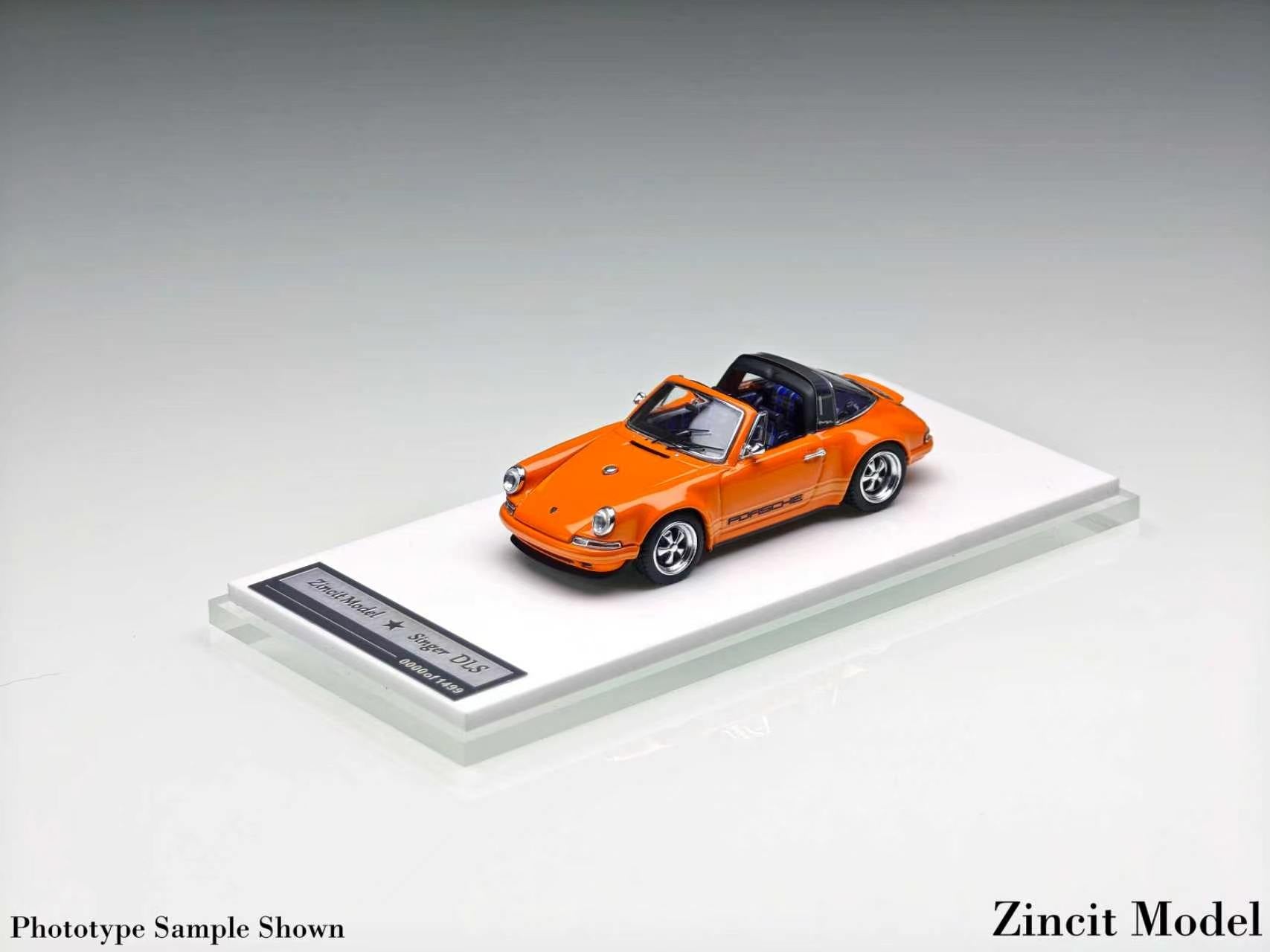 An orange miniature model of a Porsche 911 convertible, displayed on a clear acrylic stand with a black label, set against a neutral gray background.