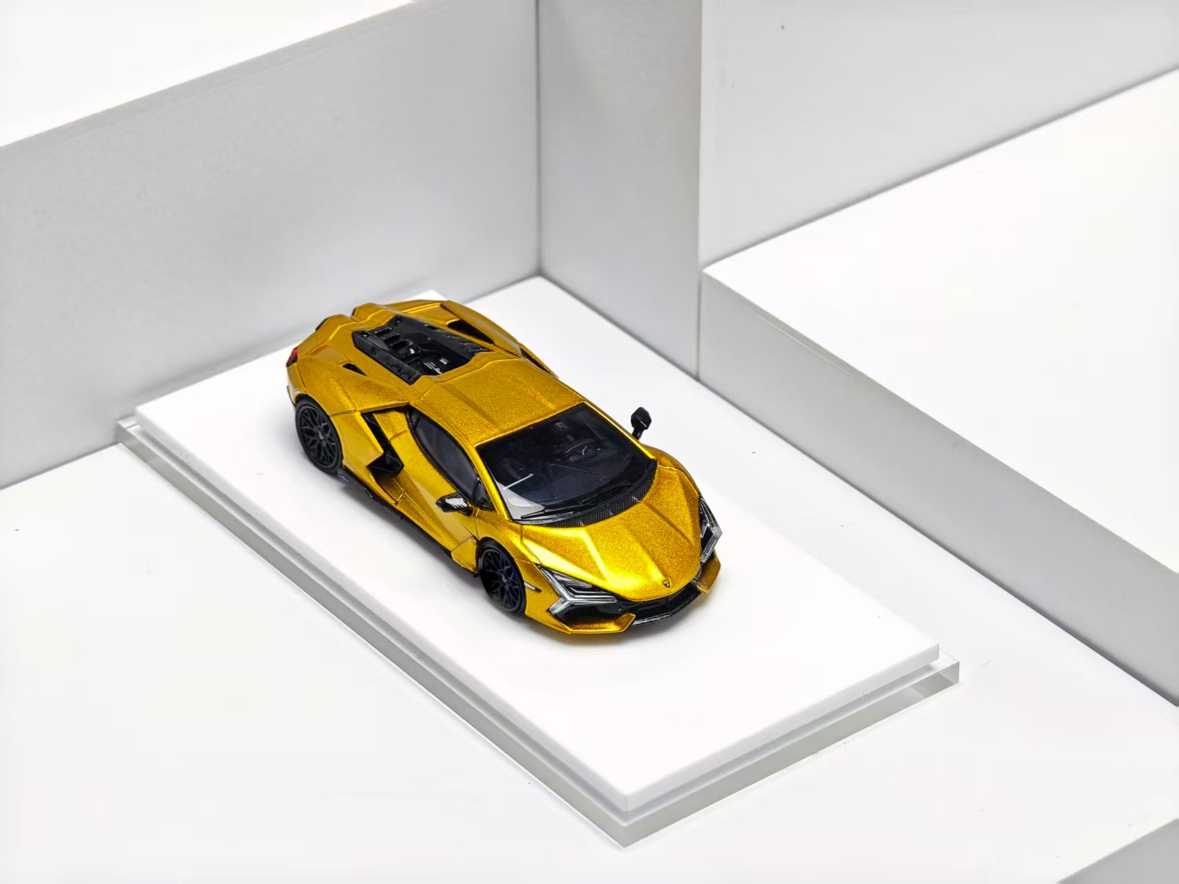 A metallic gold Lamborghini Siren model car with black accents, displayed on a white tiered platform against a clean white background.
