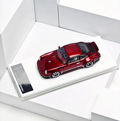 A metallic red Porsche 911 model car displayed on a white rectangular base with a small product card, photographed in a clean white geometric setting.